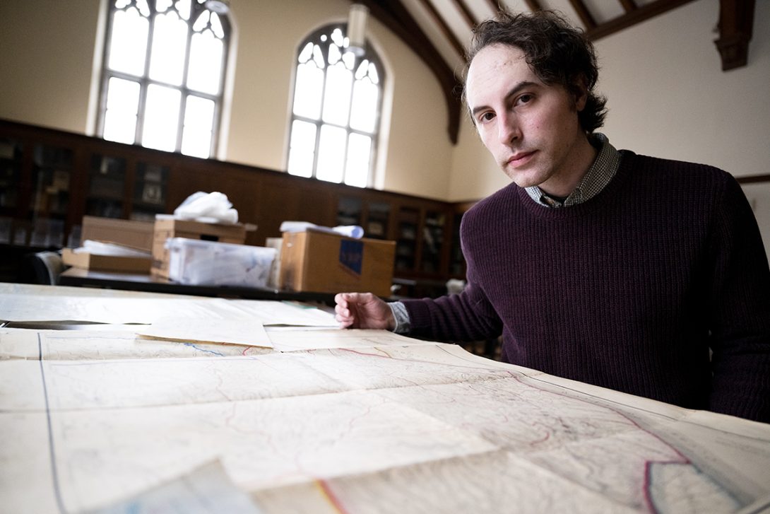 Casey Kies poses for a photo with maps on a table in front of him